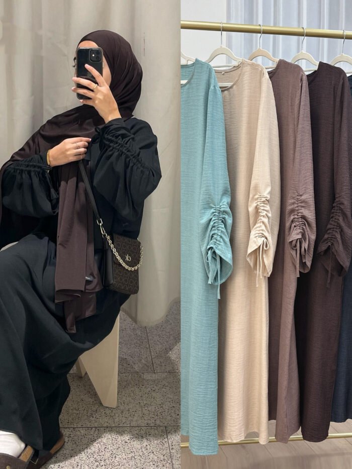 a woman taking a selfie in front of a rack of clothes, dress for hijab