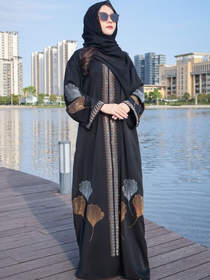 a woman wearing a black dress and sunglasses standing on a dock near water, abaya style khaleeji